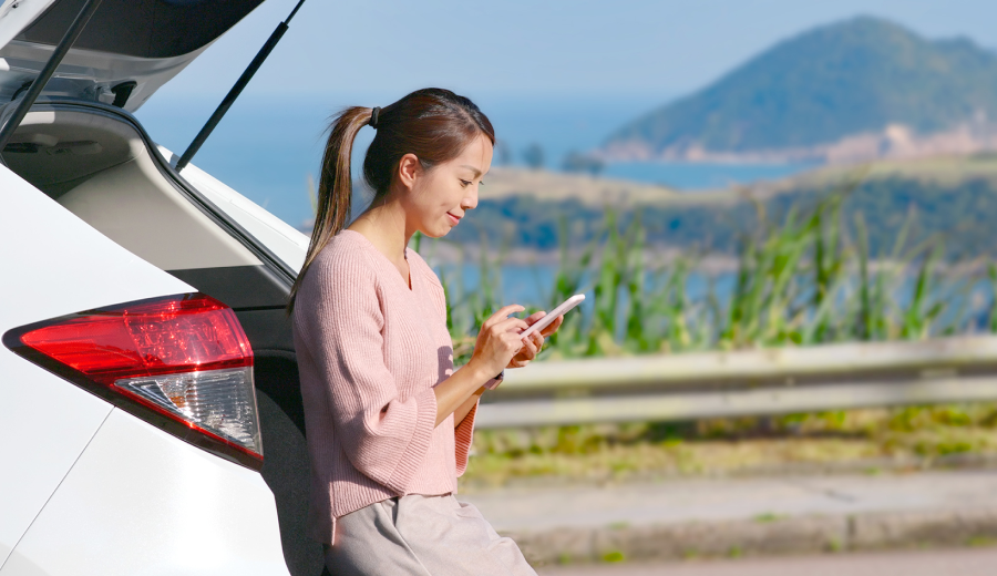 海沿いの道で車を停めてスマートフォンを操作する女性（docomo Starlink Directの利用イメージ）